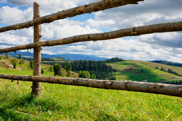 Fototapeta na wymiar fence on the hill in rural area. early autumn scenery in carpathian mountains. sunny weather with clouds on the sky. hills rolling in tho the distant mountain ridge