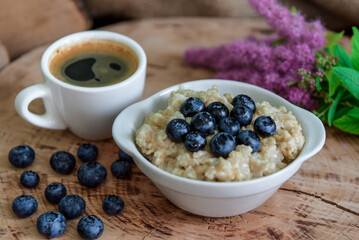 Oatmeal with blueberries for breakfast with coffee on a wooden table. Traditional healthy breakfast. Oatmeal and espresso. Close-up