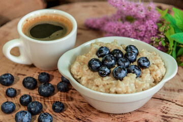 Oatmeal with blueberries for breakfast with coffee on a wooden table. Traditional healthy breakfast. Oatmeal and espresso. Close-up