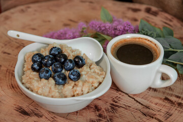 Oatmeal with blueberries for breakfast with coffee on a wooden table. Traditional healthy breakfast. Oatmeal and espresso. Close-up