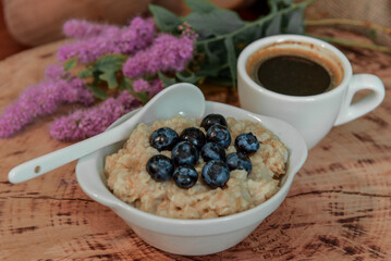 Oatmeal with blueberries for breakfast with coffee on a wooden table. Traditional healthy breakfast. Oatmeal and espresso. Close-up