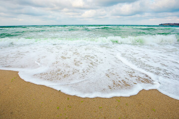 green sea waves beneath a grey sky. tide rolling on the beach. empty calm scenery. loneliness concept