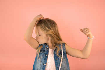 Portrait of funny cheerful little caucasian schoolgirl kissing biceps and showing strength, pink background, copy space, kids healthy lifestyle concept - obrazy, fototapety, plakaty