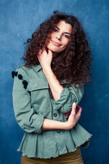 young pretty woman with curly brunette hair posing cheerful on blue background, lifestyle people concept