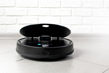 Home Cleaning Concept. Modern robot vacuum cleaner cleans houses on porcelain tiles against a brick wall. New technologies, quick house cleaning automatic robot assistant. Smart appliance for cleaning