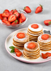 Mini pancakes with strawberries and powdered sugar on a plate on a light background