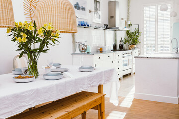 Grey plates, vine glasses and yellow flowers in vase in trendy dining room interior with wicker chandeliers