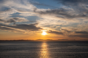 Sunrise, sunset clouds. Twilight, dusk cloudy sky over sea water, mountain silhouette