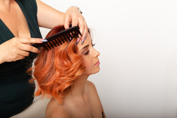 Naklejka premium Beautiful redhead woman getting her hair comb by professional female hairdresser.