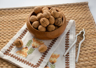 Whole walnuts in a wooden bowl. Nut cracker and embroidered fabric create a vintage look.