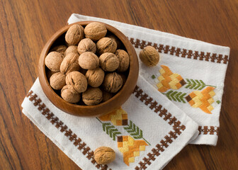 Whole walnuts in a wooden bowl. Embroidered fabric create a vintage look.