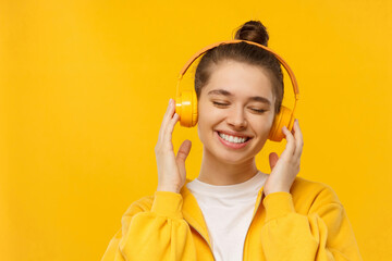 Teen girl listening to music via wireless headphones with eyes closed, isolated on yellow background