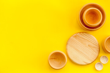 Set of rustic wooden tableware - bowls and utensils on yellow background top view