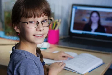 Fotobehang Online onderwijs op afstand. Een gelukkig meisje studeert thuis en maakt huiswerk voor school via internet © Albert Ziganshin
