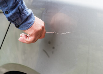 a man scratches a car with a nail