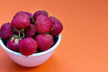 fresh tasty strawberries in a bowl against orange background. empty space for text