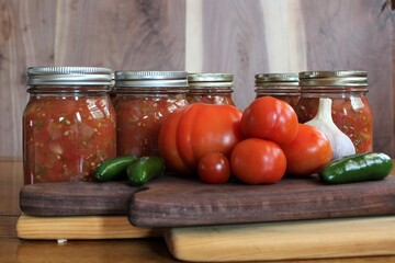 fresh tomatoes and jalapenos from a family farm vegetable garden with garlic and red onion for home canned spicy salsa in glass jars on a rustic background