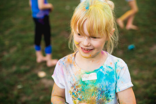 Holi Fest. Portrait of a little beautiful girl on nature on summer day vacation. child in dress is playing in the green park at the sunne time. The concept of family holiday and time together