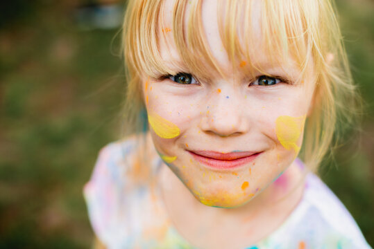Holi Fest. Portrait of a little beautiful girl on nature on summer day vacation. child in dress is playing in the green park at the sunne time. The concept of family holiday and time together