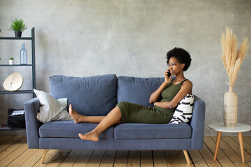 Obraz premium Unhappy African American woman talking on the phone, angry girl talking on the phone, discharged or broken mobile device, problem with phone, sitting on sofa