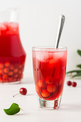 Summer delicious refreshing compote of cherries with pulp and with ice in glasses on a white background, a jug with a drink