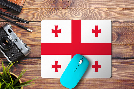 Georgia flag on wooden background with blue wireless mouse on a mouse pad, top view. Digital media concept. - Powered by Adobe