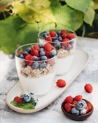 Healthy breakfast. Two glass glasses with yogurt, muesli and fresh berries are on an elongated plate. Nearby are fresh blueberries and raspberries. Summer light breakfast in nature. Healthy diet.