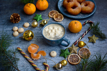 Blue mug with marshmallows, candies, mandarins, Christmas toys, donuts on a plate, cones and fir branches on a blue background.