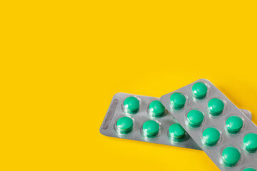 Two blisters of green pills on a yellow background.