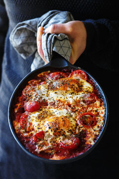 Shakshouka - Middle eastern traditional dish with poached eggs in tomato sauce, man holding pan