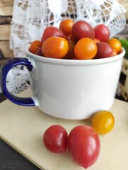 Food still life red and yellow cherry tomatoes in a ceramic bowl on a wooden table with a lace napkin