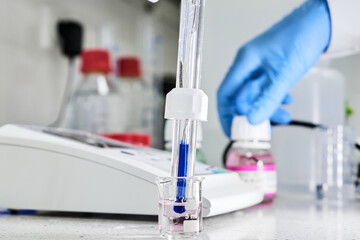 Woman in a rubber gloves holding a glass electrode for measuring of pH of the solution using pH...
