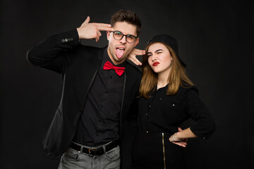 Teenage smiling rap couple in black clothing and a black cap show signs with their hands and tongue. Isolated colors on a black background