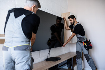 Two professional technicians, workers in uniform installing television on the wall indoors....