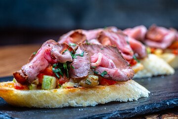 Bruschetta with ham or roast beef is on a slate plate.