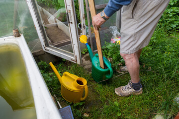 an elderly male gardener stirring plant fertilizer in a watering can 