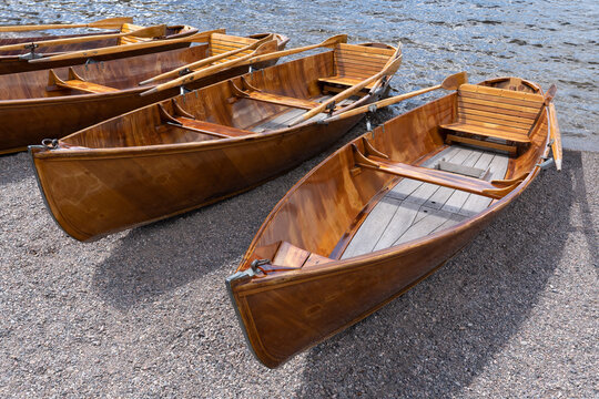 Ruderboote aus Holz liegen nebeneinander im feinen Kies am Ufer eines Sees