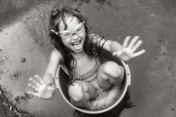a girl in swimming glasses splashes water while sitting in a basin on the street. black-white