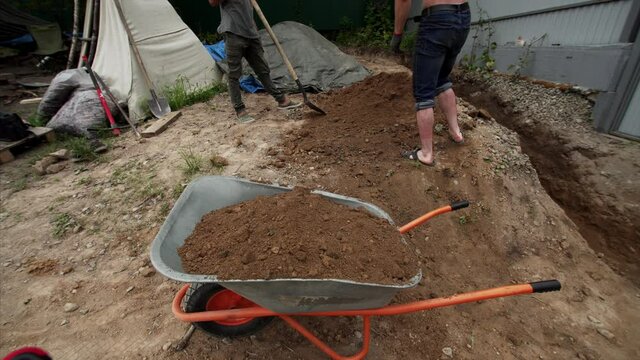 Great timelapse of two laborers collecting soil left after digging a ditch into the wheel barrow for transportation it into another site of the garden