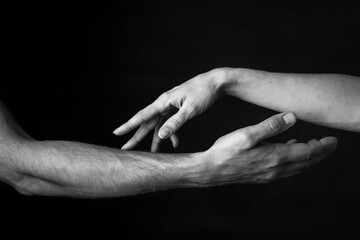 male and female hands touch each other on a dark background. close up. black and white photo