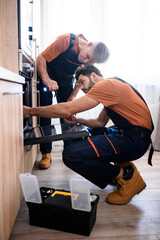 Get the best Handyman service. Full length shot of two repairmen, workers in uniform examining oven using screwdriver and flashlight indoors. Repair service concept