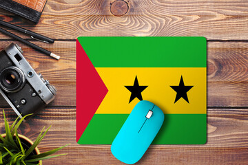 Sao Tome And Principe flag on wooden background with blue wireless mouse on a mouse pad, top view....