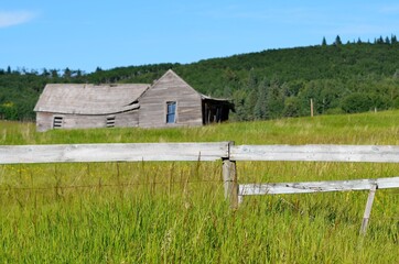 Old abandoned farm house with a faded white fence in front  