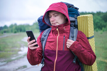 Hiker traveler with a large backpack is looking at a map in his smartphone.