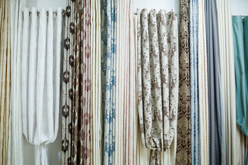 Curtain samples hanging from hangers on rail in store. Fabric texture samples selection fabrics for interior decoration Curtains, tulle and furniture upholstery.