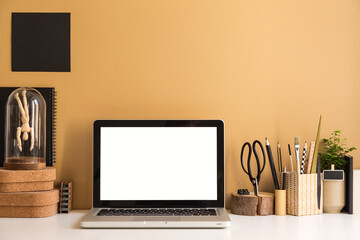 Laptop at workspace with wooden and cork accessories against bright brown wall.