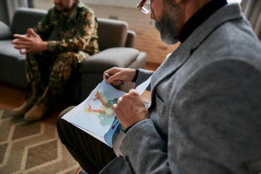 Mature psychologist choosing picture with ink stain, Rorschach Inkblot during therapy session with military man. Soldier suffering from depression, psychological trauma. PTSD concept