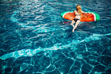 Young hot woman resting at swimpool. Back view picture of relaxed slim woman in black swimsuit lying on swim ring in water and has fun. Woman swimming alone at resort spa place in summer.