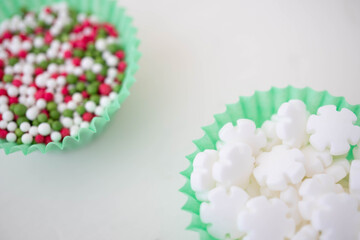 Two cup cake cases filled with cake decoration sprinkles in bright fun colours.  Macro shot of home baking concept against a white background with space for copy text