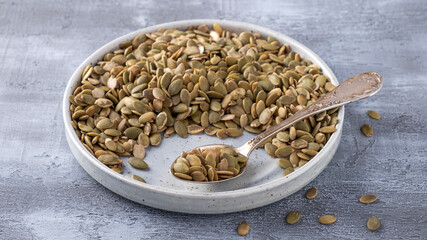 Raw organic pumpkin seeds in a spoon and  plate on grey backgrouns. Pumpkin seeds